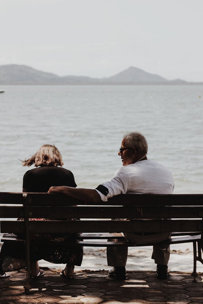 Senior couple enjoying a serene moment by the seaside, sitting on a bench with a scenic ocean view.